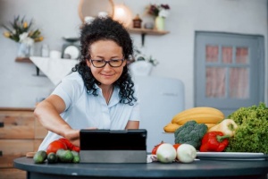 woman with glasses in kitchen reading tablet 